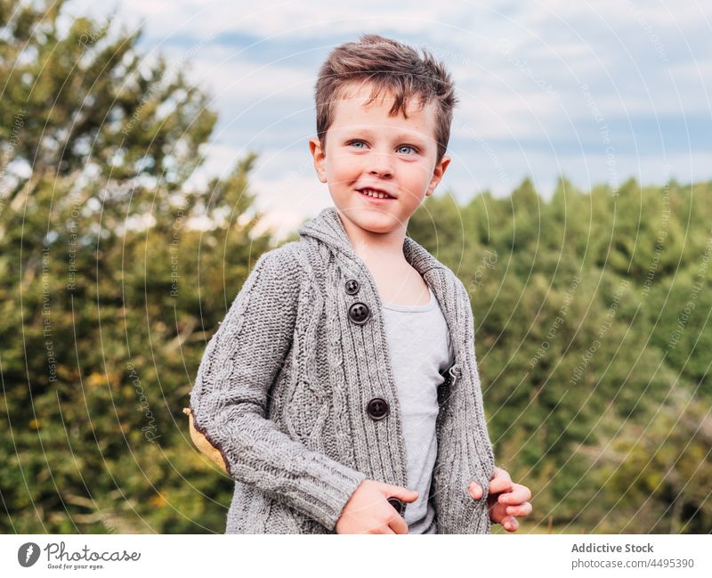 Cute little boy smiling and looking away in nature smile mountain cardigan forest tree countryside child positive portrait happy childhood cloudy sky adorable