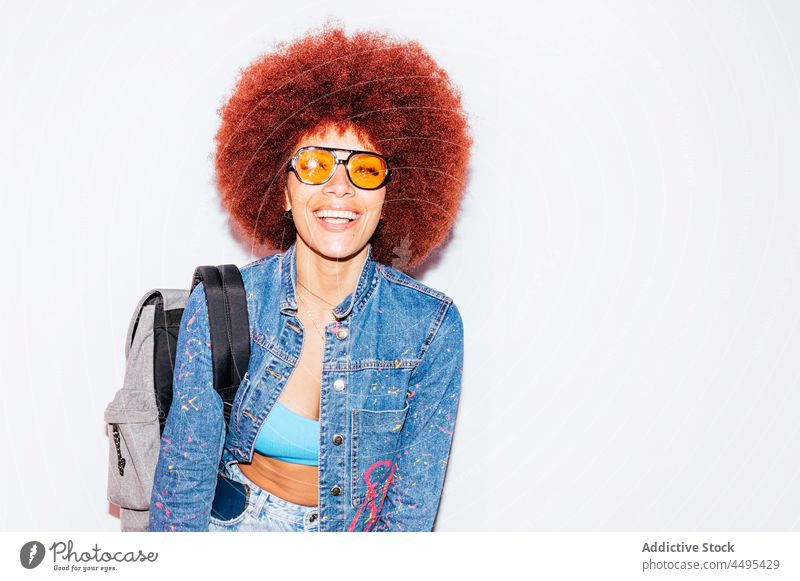 Cheerful woman with Afro hairstyle and a backpack afro fashion trendy apparel wall appearance outfit female street sunglasses accessory top attractive denim