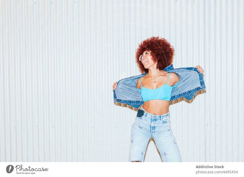 Happy woman in denim outfit near wall afro style fashion trendy apparel having fun carefree mood appearance female street hairstyle sunglasses accessory top