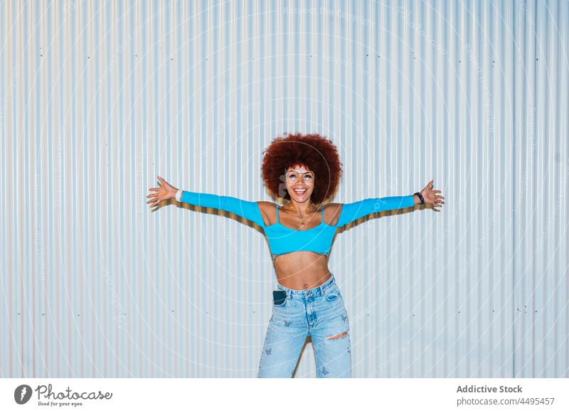 Fashionable smiling woman with Afro hairstyle standing near wall afro fashion trendy apparel appearance outfit street female sunglasses accessory top attractive