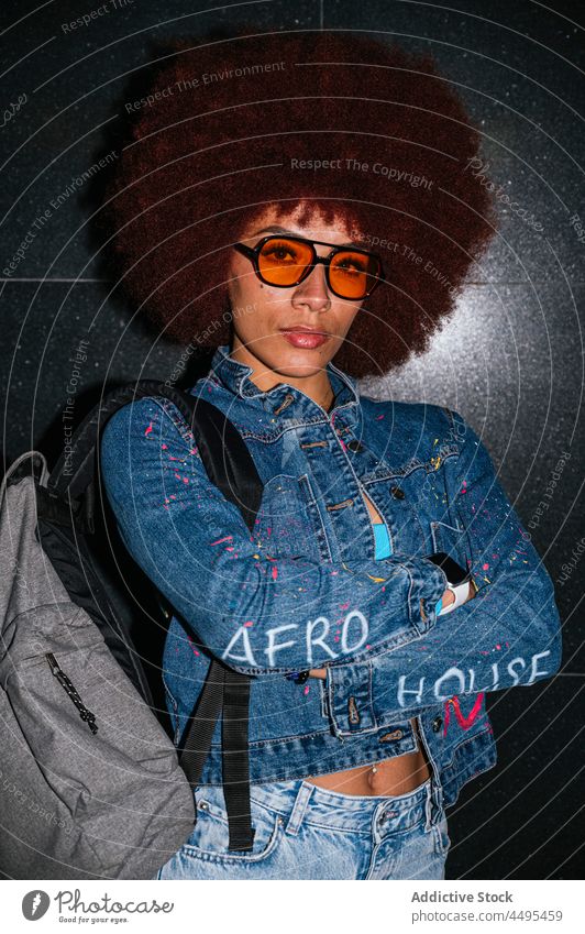 Serious woman in stylish wear on dark street denim afro style fashion apparel street style backpack evening twilight female hairstyle sunglasses eyewear design