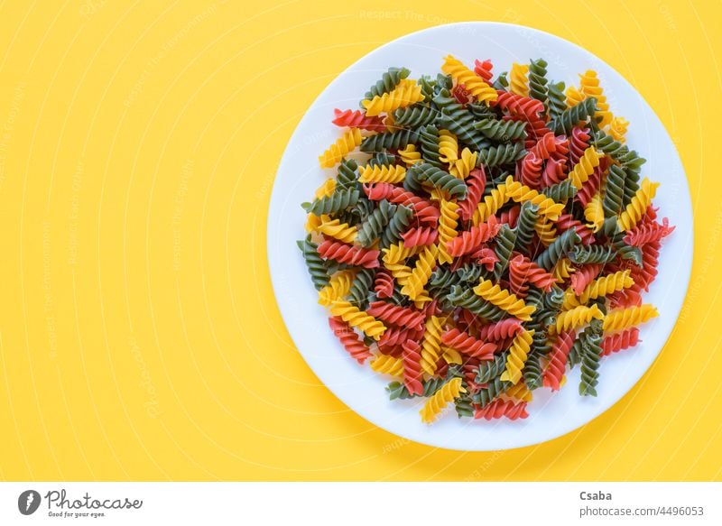 Red green and yellow dry raw fusilli pasta on a plate with yellow background and copy space. uncooked colorful dried noodle noodles food italian red copyspace