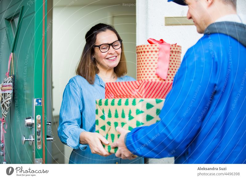 Delivery man bringing holiday packages. Woman at home standing in doorway, receiving parcels for Christmas gifts. christmas delivery happy deliveryman present