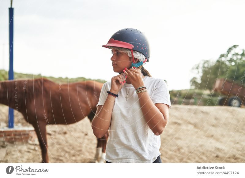 Girl putting on jockey cap near horses in ranch girl teenage animal put on stable farm helmet countryside stand daytime equine casual equestrian fence mammal