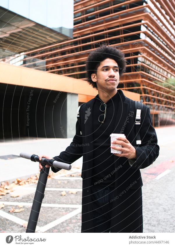 Trendy ethnic guy with scooter drinking takeaway coffee on street man style self assured elegant african american man fashion appearance city trendy male young