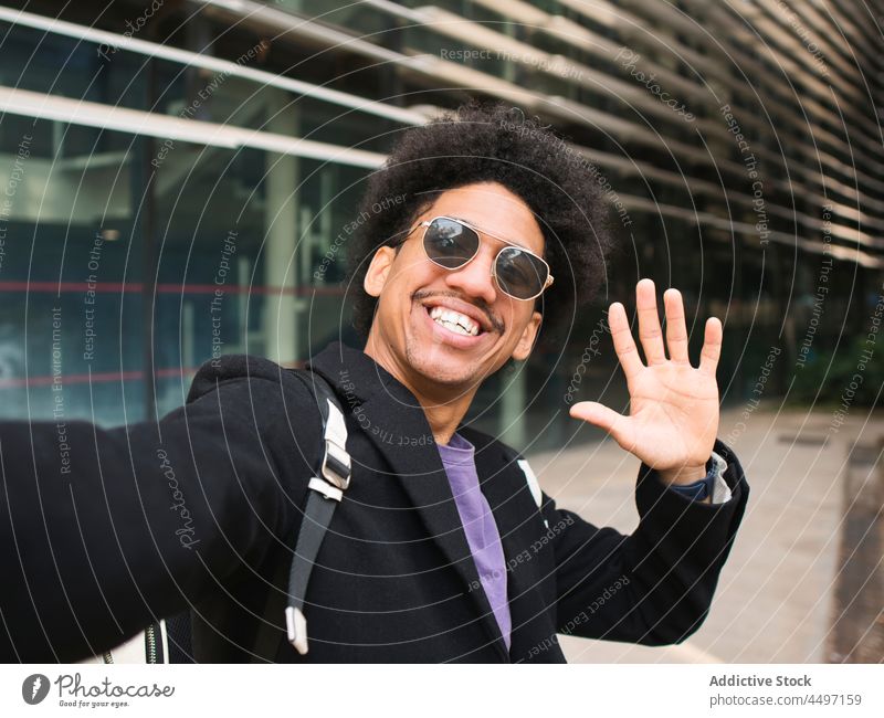 Cheerful black man smiling happily while taking selfie smile cheerful wave hand trendy self assured style optimist city confident modern male young ethnic