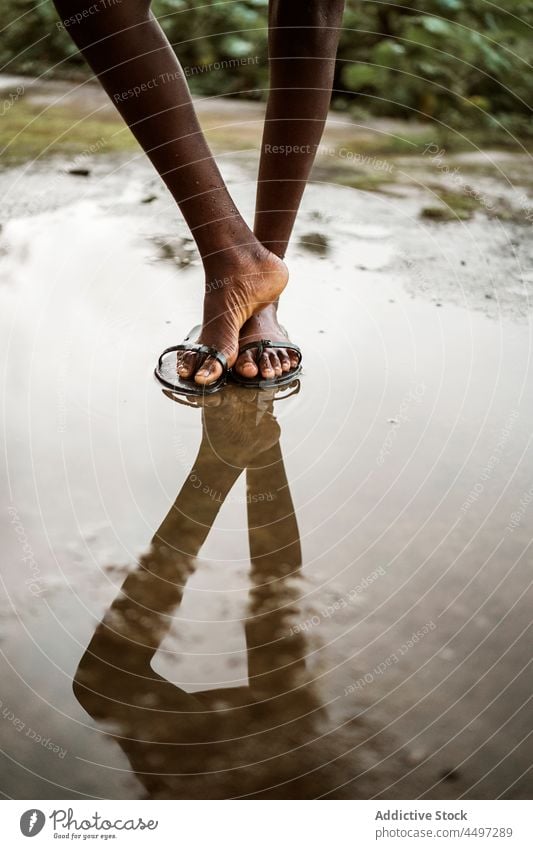 Black barefoot kid standing in puddle on street wet asphalt road water sidewalk flip flop sandal São Tomé and Príncipe africa african child black reflection