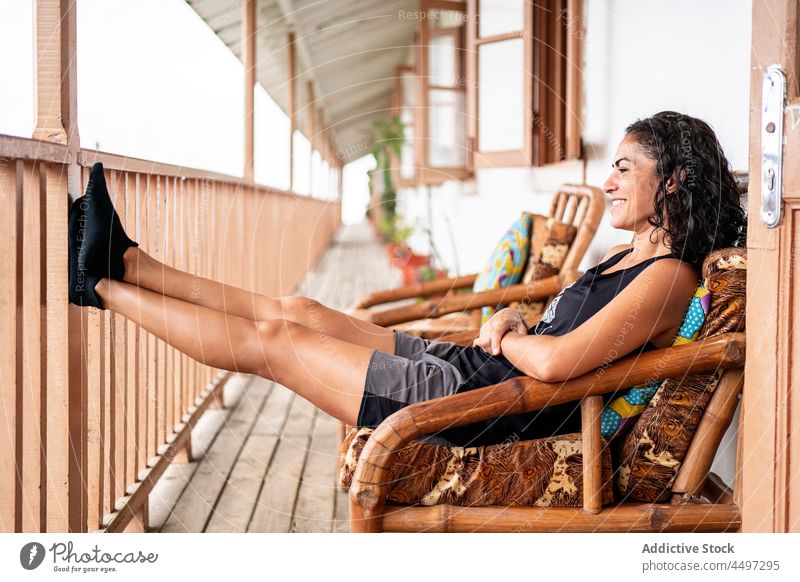 Happy ethnic woman resting on terrace and smiling smile cheerful vacation tourist house holiday armchair enjoy trip happy female young brunette casual