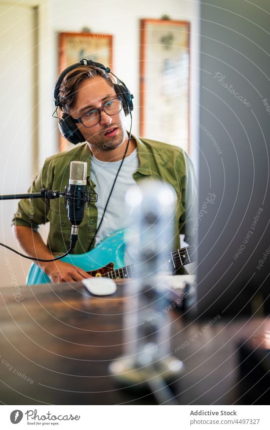 Guitarist holding instrument and using computer in studio man guitarist headphones musician microphone melody talent male record skill content focus sound