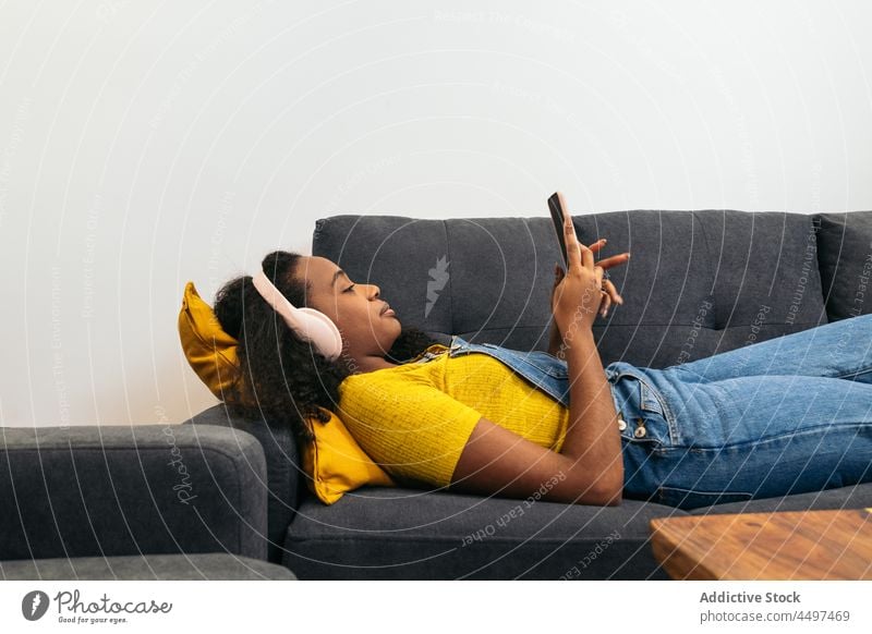 Black female in headphones on smartphone in room woman curly hair browsing lying positive blogger listen music text message african american watch black teen