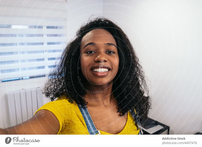 Smiling black female talking selfie in light room woman smartphone cheerful positive smile gadget device take photo blogger african american curly hair