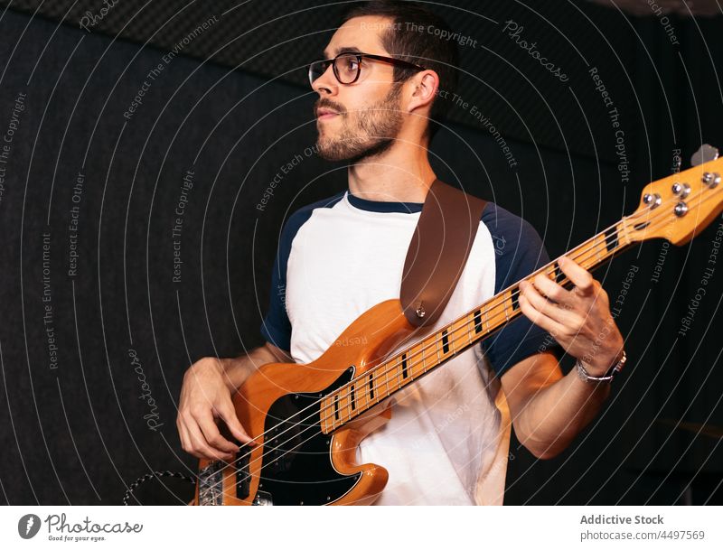 Male musician playing bass guitar in studio man instrument club perform hobby talent event male young casual glasses light confident eyeglasses artist melody