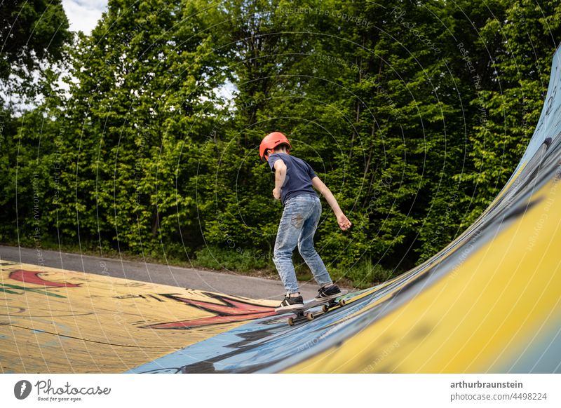 Boy in jeans and helmet riding skateboard in half pipe in outdoor skate park Boy (child) daylight Asphalt Movement boardsport Cool deck free time graffiti