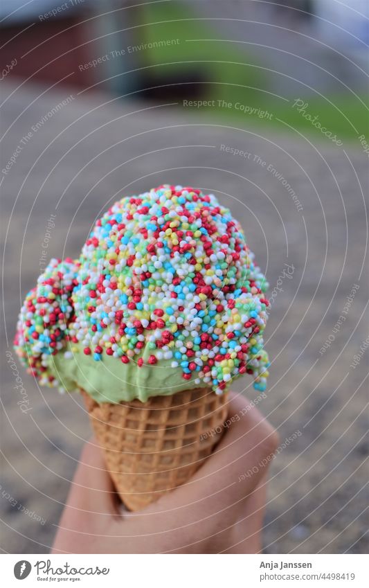 Ice cream with colorful sugar sprinkles in hand as a close-up ice cream food sweet colour tasty cold background grey blurred blurry human hand body part summer