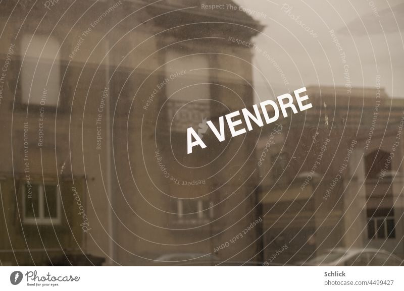 Reflection of some dwellings in a shop window with inscription a vendre a vendour Text for sale Shop window reflection Apartment Building Subdued colour Gray