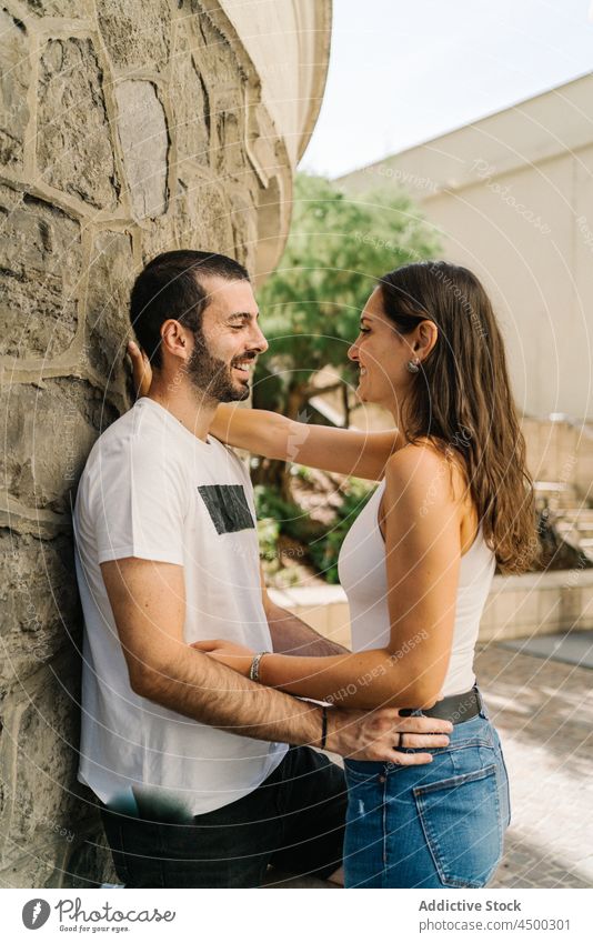 Amorous young Hispanic couple cuddling near aged stone wall in city embrace smile date love romantic relationship affection park together hug building lean on