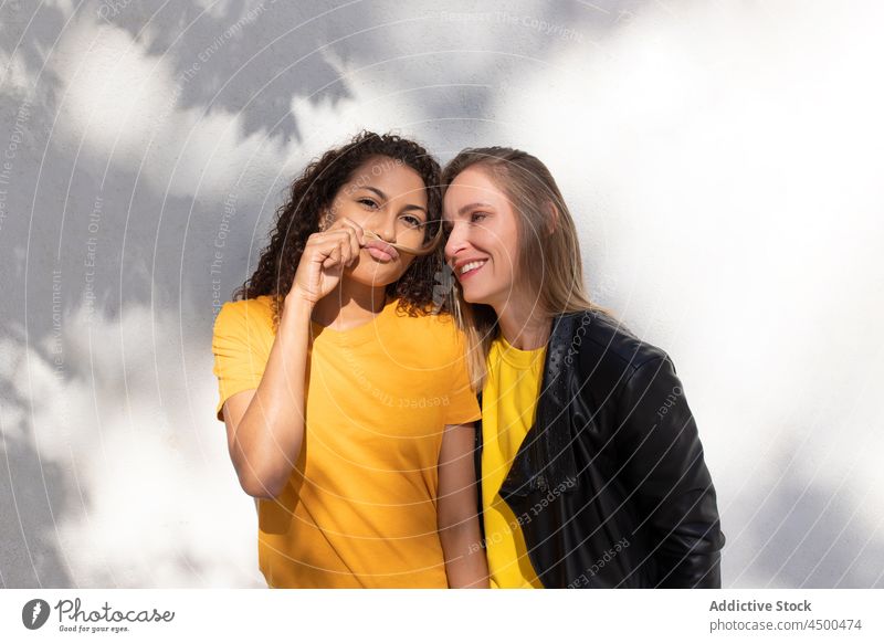 Delighted young diverse women having fun together near white wall pouting lips mustache friend joy smile happy friendship cheerful optimist positive multiethnic