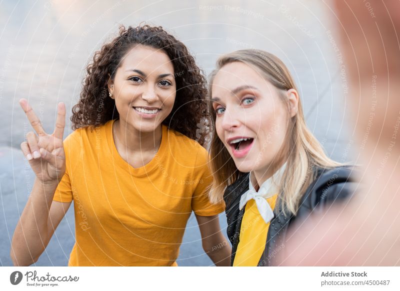 Cheerful young multiracial women smiling and taking selfie on street smile two fingers friend together spend time happy gesture v sign friendship joy casual