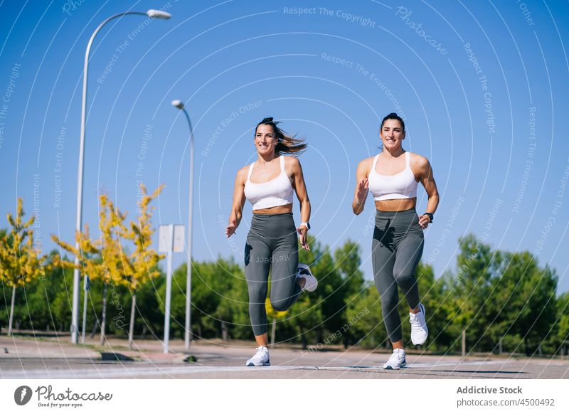 Content twin sisters jogging on asphalt women run fit fitness activity sporty together lifestyle female slim sibling wellbeing lady smile sportswear