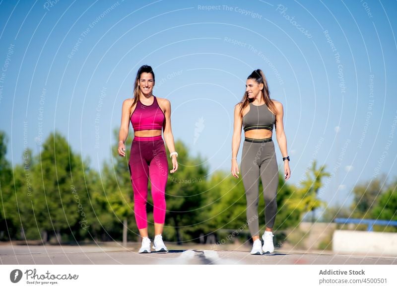 Cheerful sporty twins standing on asphalt start running jog fit fitness training women ponytail sister together cheerful positive activity lifestyle smile