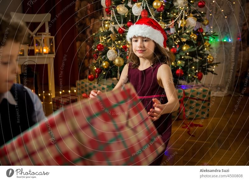 Excited cute kids happily smiling, opening Christmas gifts. Beautifully decorated living room with lights and Christmas tree. Children having fun, celebrating family holiday