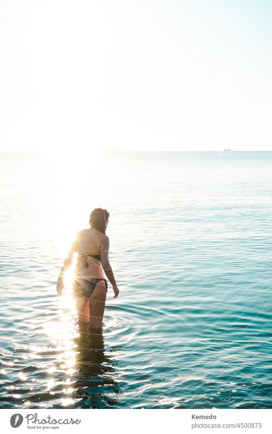 Woman entering the sea for a swim during sunrise with beautiful light. dawn beach background copy space woman young early water bath sunny white brightness