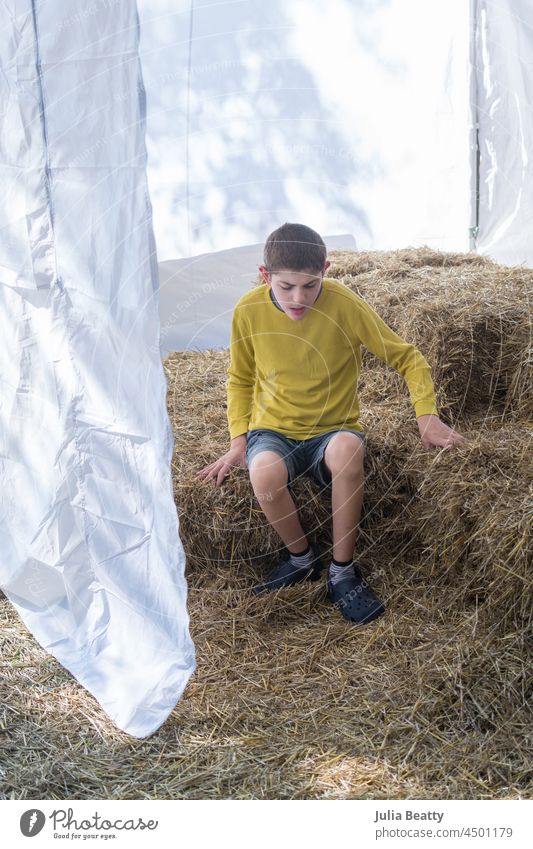 Young boy with Autism sits on bales of hay at a fall festival; sensory play and exploration autumn tent pumpkin patch farm celebrate autism special needs child