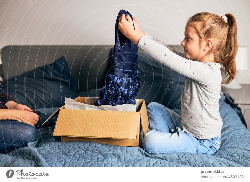 Mother and her daughter opening box with ordered dress. Online shopper customer holding dress online shopping unpacking gift present girl package home buy