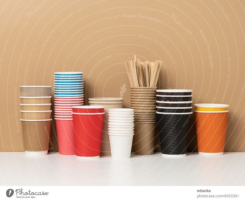 stacks of assorted disposable paper cups for drinks, coffee and tea on a white table. Takeaway beverage container americano blank blue breakfast brown cafe