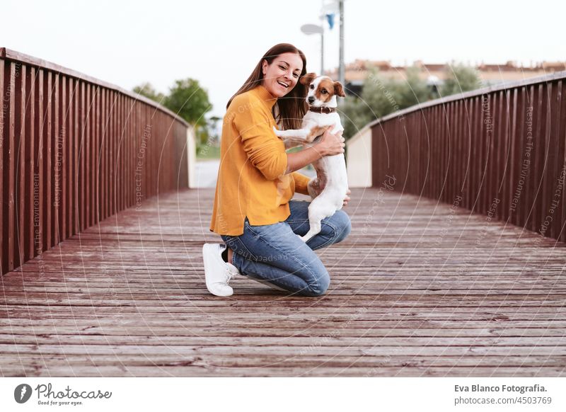 happy caucasian woman having fun with jack russell dog in park,woman and pet standing on wooden bridge during autumn season. Pets and love concept kiss enjoy