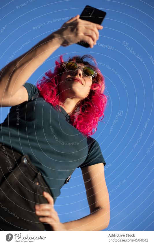 Stylish woman browsing smartphone against sky street blue sky internet online pink hair text message style surfing sunlight female cellphone vivid mobile