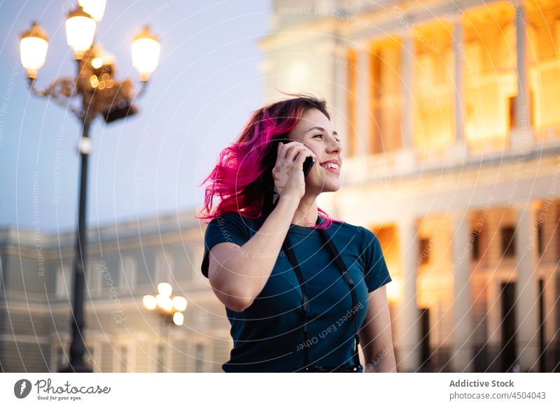 Positive woman phone calling near historic building smartphone street aged classic internet online pink hair style female cellphone mobile lifestyle summer