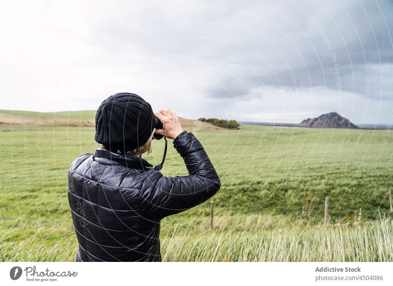 Anonymous male traveler photographing nature on photo camera standing on grassy meadow man take photo mountain explore landscape photographer tourism journey
