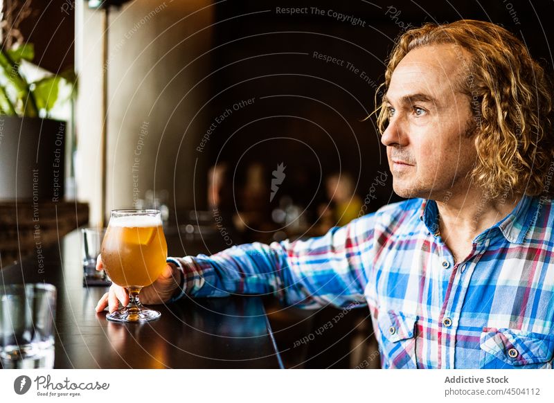Pensive man drinking beer in bar in daylight alcohol thoughtful beverage pensive pub sit male casual glass calm curly hair restaurant serious daytime guy alone