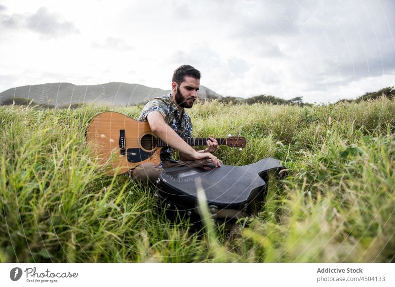 Guitarist sitting in field against hill in countryside man musician acoustic guitar grass instrument nature male cloudy calm guitarist harmony daylight