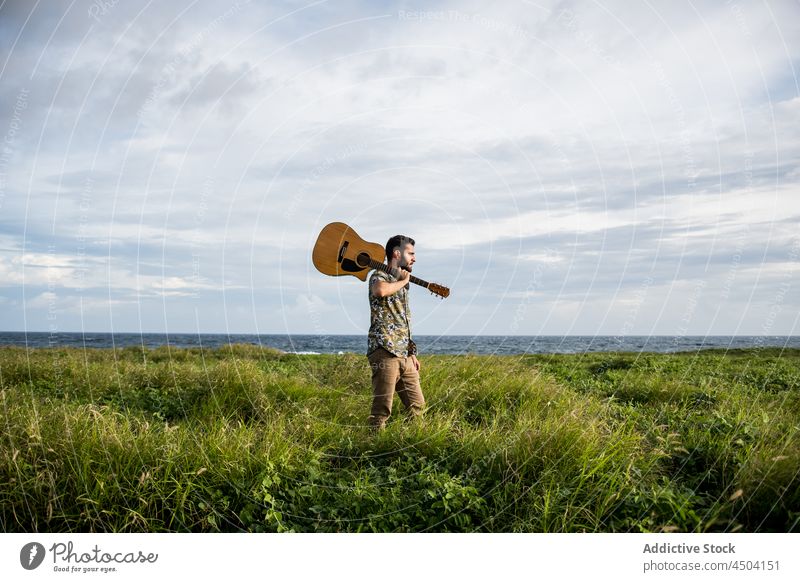 Musician standing with guitar on grassy shore against wavy sea man play musician ocean acoustic instrument guitarist male daylight coast green seashore beach