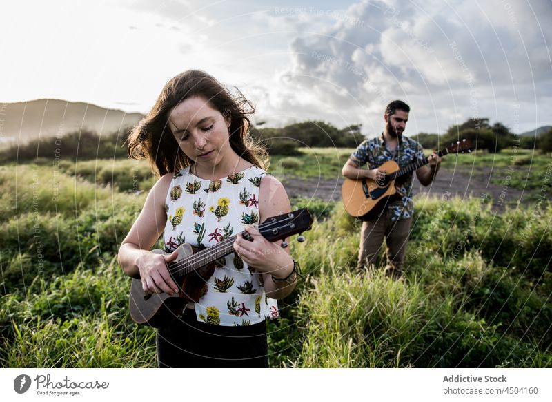 Friends musicians standing in field and playing guitar woman ukulele instrument nature friend female acoustic calm casual concentrate together guitarist hobby