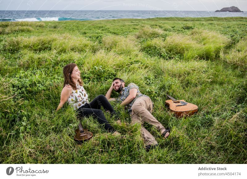Musicians with guitar and ukulele lying on grass near sea in daylight woman friend music instrument nature coast guitarist female daytime play ocean happy shore