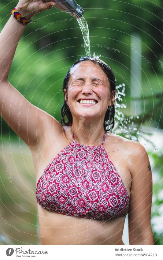 Cheerful woman pouring water on head in summer time bottle park tree happy cheerful wet hair female top eyes closed nature smile laugh delight season content