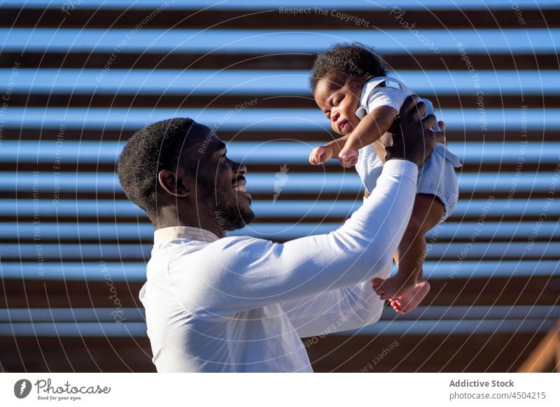 Black father carrying little kid on hands man baby parent child happy fatherhood lift dad male african american black street childhood parenthood smile joy glad