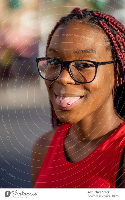 Cheerful black female showing tongue with piercing in sunlight woman braid positive street glad tongue out style trendy optimist african american happy
