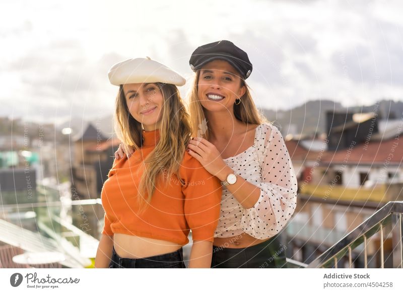 Happy female friends hugging on street women style cap trendy cheerful together happy embrace bonding smile content casual carefree fair hair pleasant blond