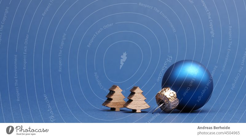 Blue Christmas tree ball with small wooden tree shapes on a blue paper background merry christmas bauble nobody wishing seasonal decoration wishes gold
