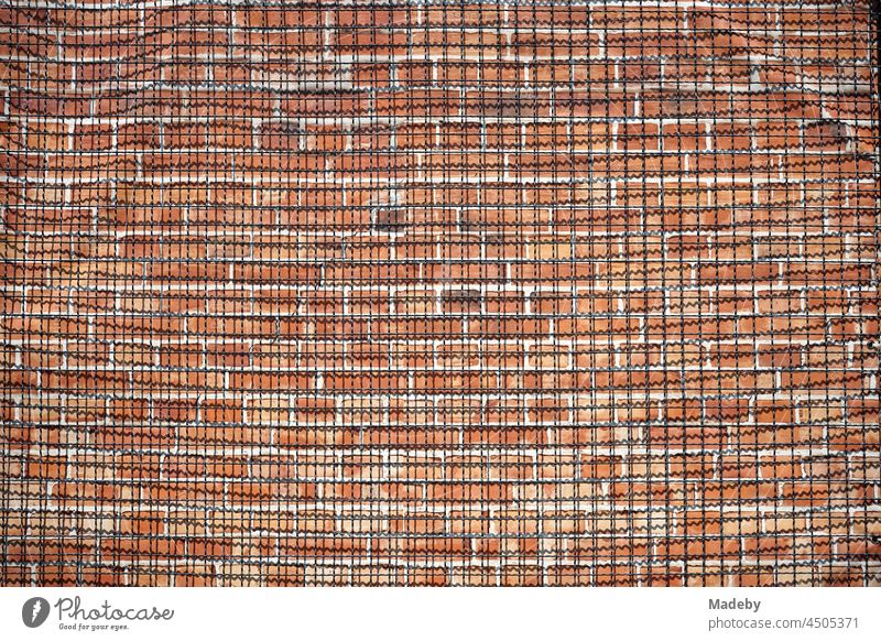 Wire fence in front of an old reddish-brown brick wall in summer sunshine at Klassikstadt in the district of Fechenheim in Frankfurt am Main in Hesse, Germany