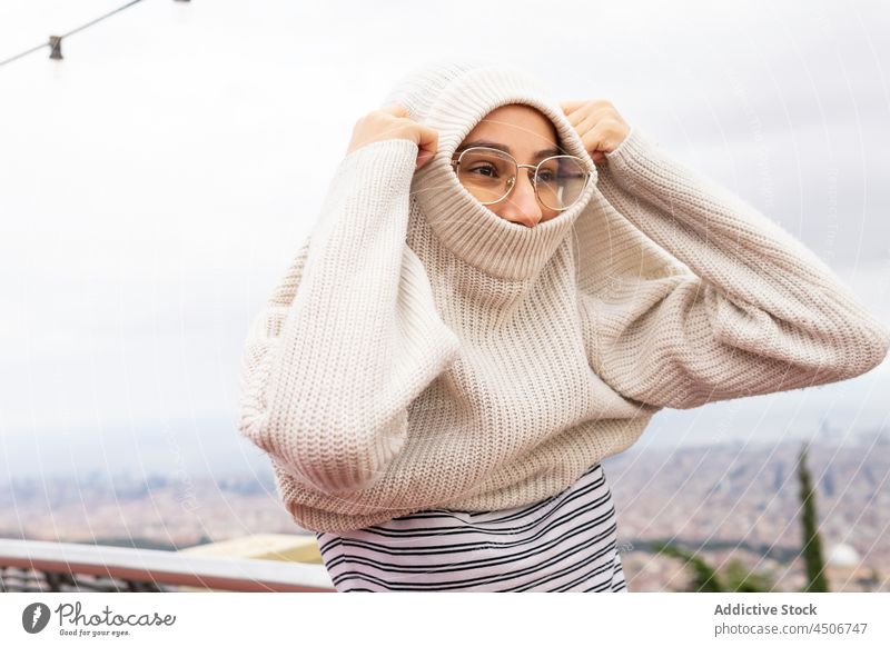 Woman putting on warm sweater woman viewpoint city put on cold wind weekend positive season dress up knitwear cozy content glasses style urban eyewear town