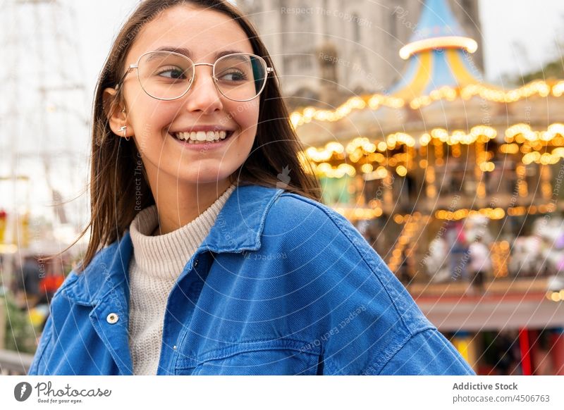 Smiling female near carousel in city park woman railing street positive building glasses lean on hand lifestyle young smile town metal stand urban casual