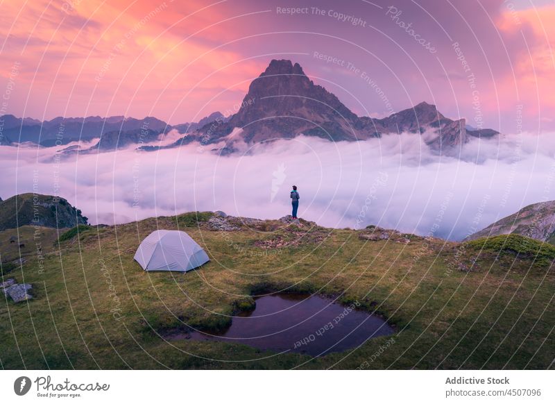 Unrecognizable traveler on grassy field with tent on mountain above clouds tourist cliff adventure nature hiker fog camping evening sunset sundown pyrenees