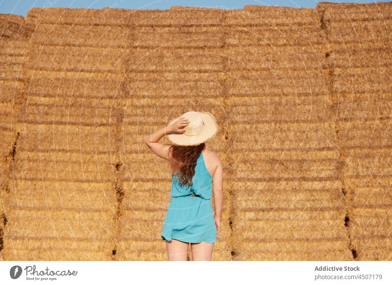 Back view of woman with hat near haystacks wind laugh flip hair fun expressive rural playful joy female positive glad cheerful optimist dry lady pleasure straw