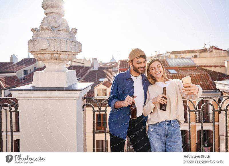Smiling friends drinking beer and staking selfie man woman using smartphone positive share balcony online female glass internet cellphone alcohol bottle fence