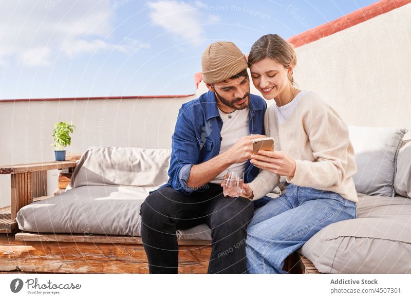 Smiling couple using smartphone together on couch watch share terrace connection online internet search man woman boyfriend girlfriend browsing sofa gadget